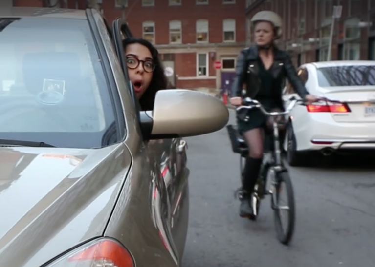 Huff Post video gag shot for We Aspire Facebook posting of video. Woman driver looking at side view mirror aghast to see oncoming woman cyclist.