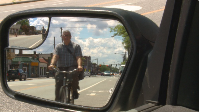 Cyclist viewed in left side mirror from WKYC Investigator news report on Doorings. Twitter image for Investigator | Bicyclists, car doors collide with painful results. July 10, 2017 WKYC Channel 3 News. Cleveland, OH, USA.