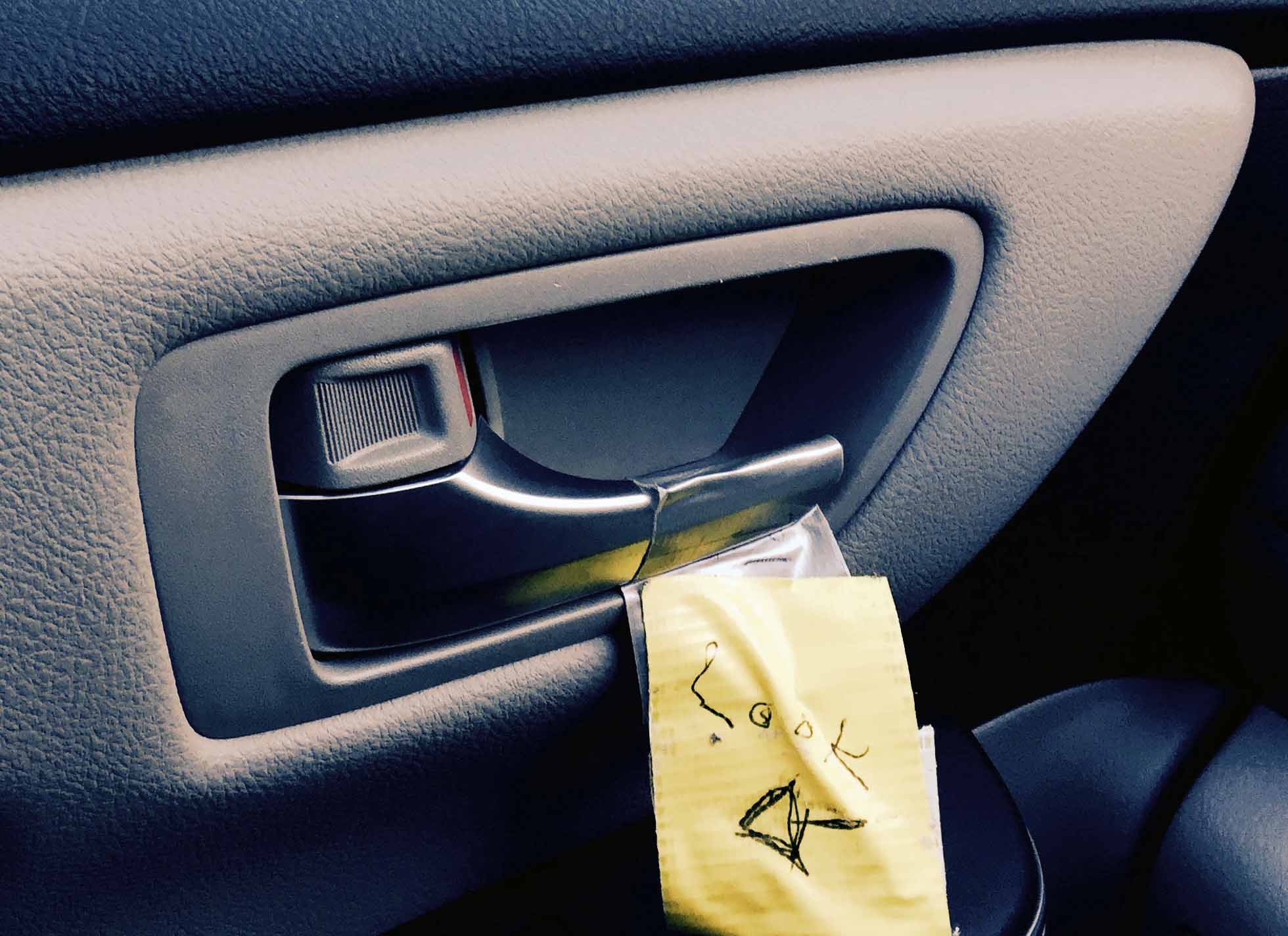 A note is taped next to car door latch with arrow pointing to latch & word "Look" printed on it. Note is to remind driver or passenger to use the safer far hand Dutch Reach method to exit vehicle to avoid dooring a cyclist who might otherwise crash into or hit the door were it suddenly opened.