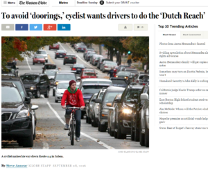 Photo of a young man cyclist riding on heavily traffic'd street in Salem, MA, USA, no helmet, wearing red jacket.